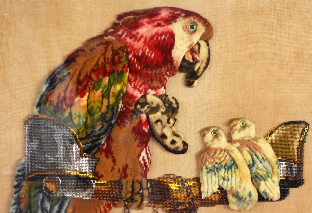 A dark carved wood Victorian fire screen framed around a central needlepoint panel depicting a parrot perched above two dogs. View XI