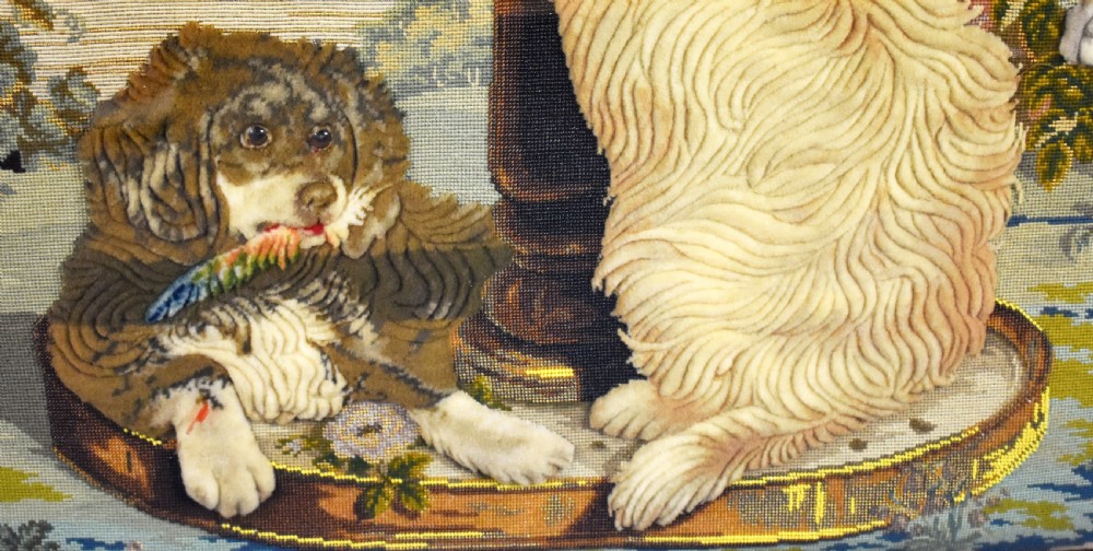 A dark carved wood Victorian fire screen framed around a central needlepoint panel depicting a parrot perched above two dogs. View XVII