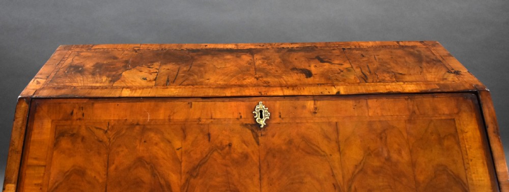 A George I walnut slant-front bureau featuring figured wood veneers, engraved brass hardware, multiple drawers, and turned bun feet. View XII