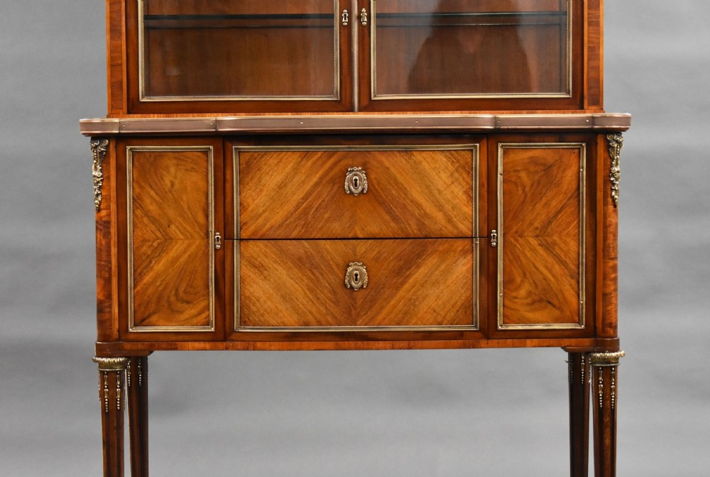 A 19th-century French walnut cabinet featuring a two-door glazed top display section above a lower storage unit with drawers and brass mounts, raised on tapered legs. View IV