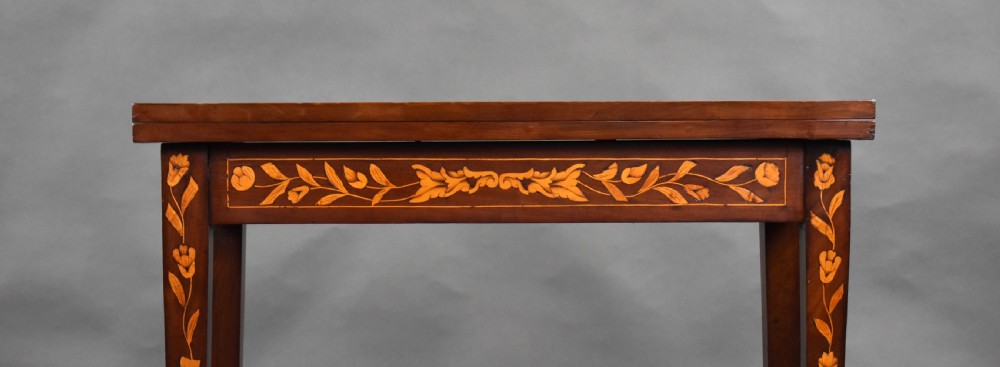 A 19th-century Dutch mahogany card table decorated with detailed floral marquetry inlay across the folding top, apron, and tapered legs. View IX