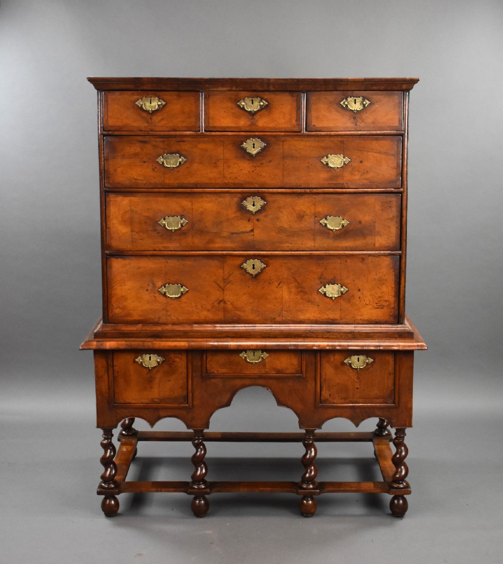 An eighteenth-century George II burr walnut chest on stand featuring multiple brass-handled drawers, shaped apron, barley twist legs, and connecting stretchers.