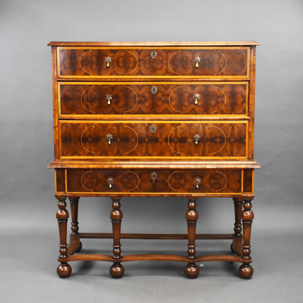 A William and Mary period walnut chest on stand featuring intricate oyster veneering, boxwood inlay, drop brass handles, six turned legs, and a wavy stretcher.