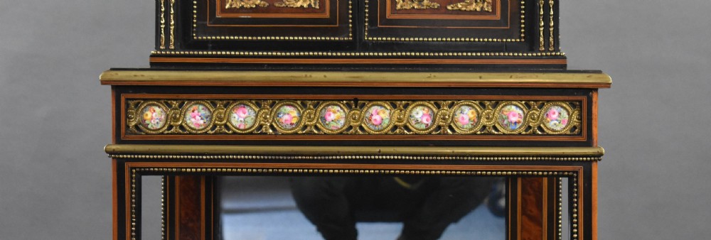 A 19th-century French bonheur du jour writing desk featuring ebonised wood, burr walnut panels, gilt-bronze mounts, oval porcelain plaques, and an open lower tier. View V