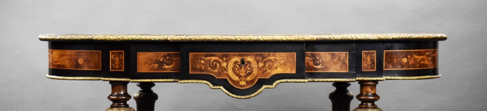 A 19th-century shaped oval marquetry centre table featuring detailed floral wood inlay, ebonised borders, gilt bronze mounts, and turned legs with a central urn finial stretcher. View XI