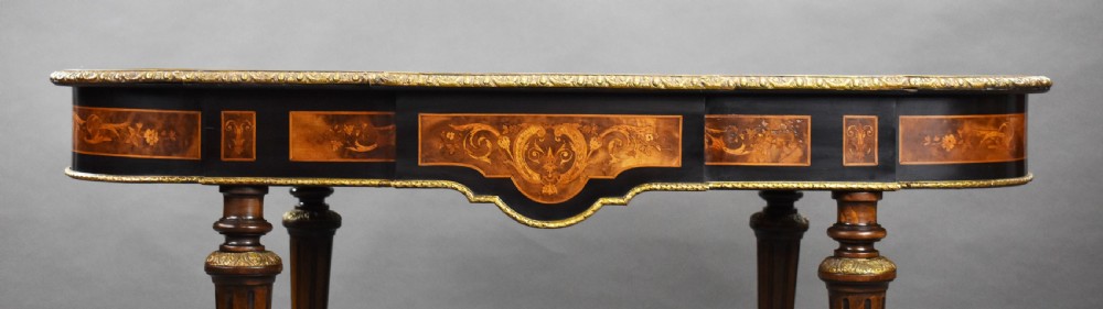 A 19th-century shaped oval marquetry centre table featuring detailed floral wood inlay, ebonised borders, gilt bronze mounts, and turned legs with a central urn finial stretcher. View XVII