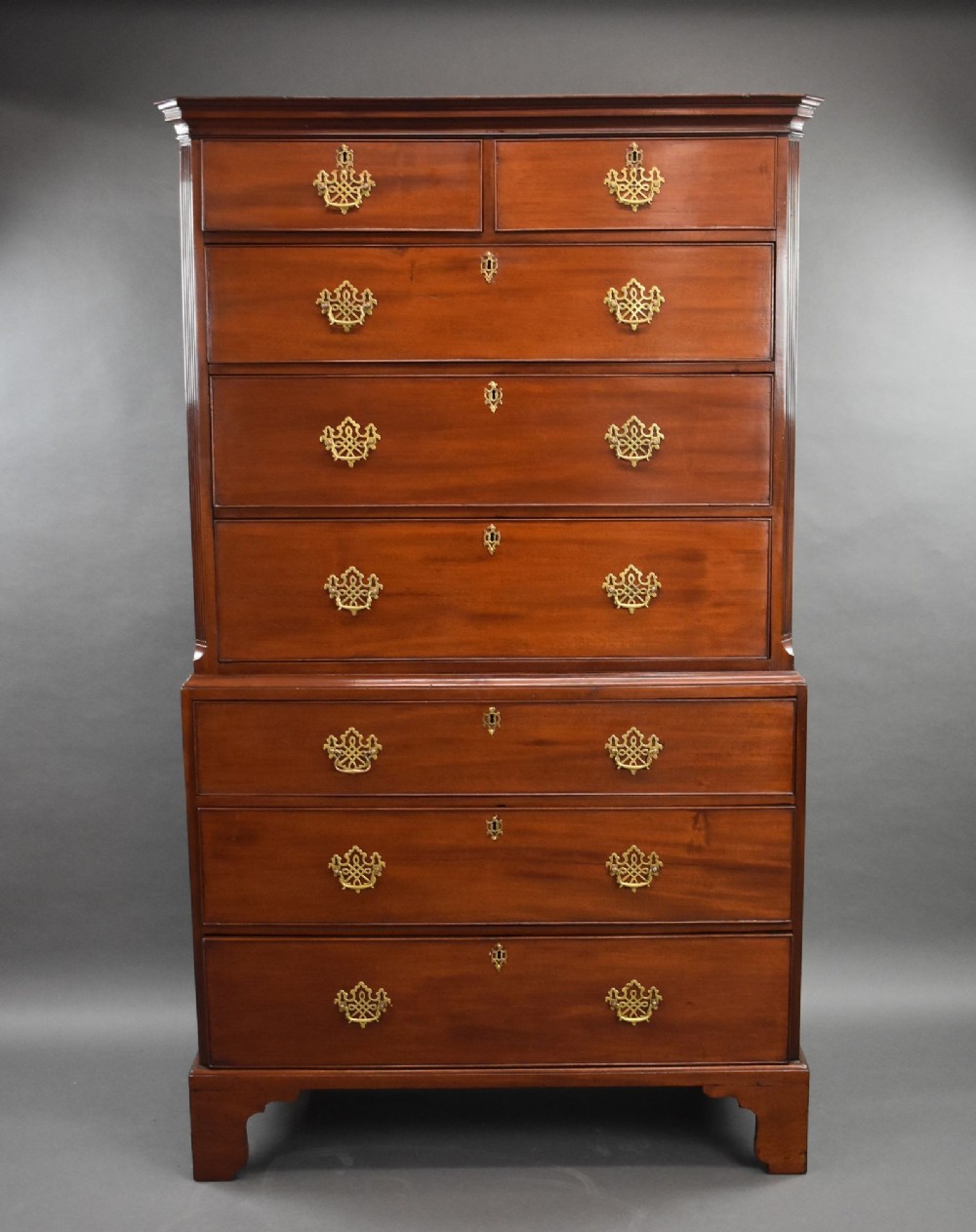 A George III mahogany chest on chest featuring two short over six long graduated drawers with ornate brass handles and bracket feet.