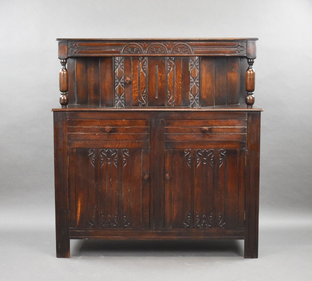 A dark oak sideboard buffet featuring carved panel doors, two drawers, turned gallery supports, and decorative tracery detailing throughout.
