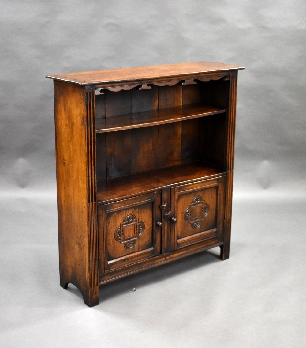 A freestanding dark oak bookcase featuring an open upper shelf section and a lower enclosed cupboard with carved geometric panel doors.