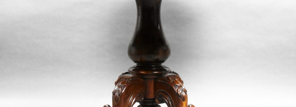 A Victorian rosewood oval tilt-top loo table shown tilted vertically to display its figured grain, supported by a carved central pedestal with four scrolling legs on castors. View IV