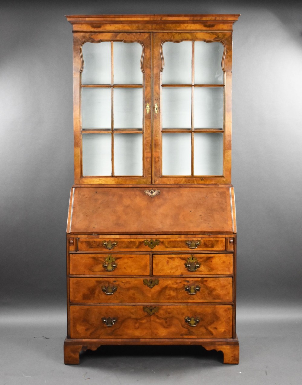 A tall George III walnut bureau bookcase featuring glazed upper cabinet doors, a fall-front writing desk, and multiple graduated drawers below.
