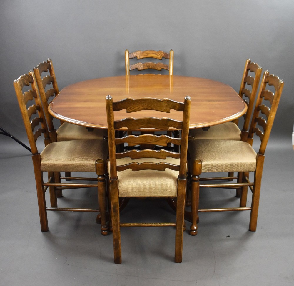 An extendable round oak dining table surrounded by six matching ladder back chairs with upholstered seats.