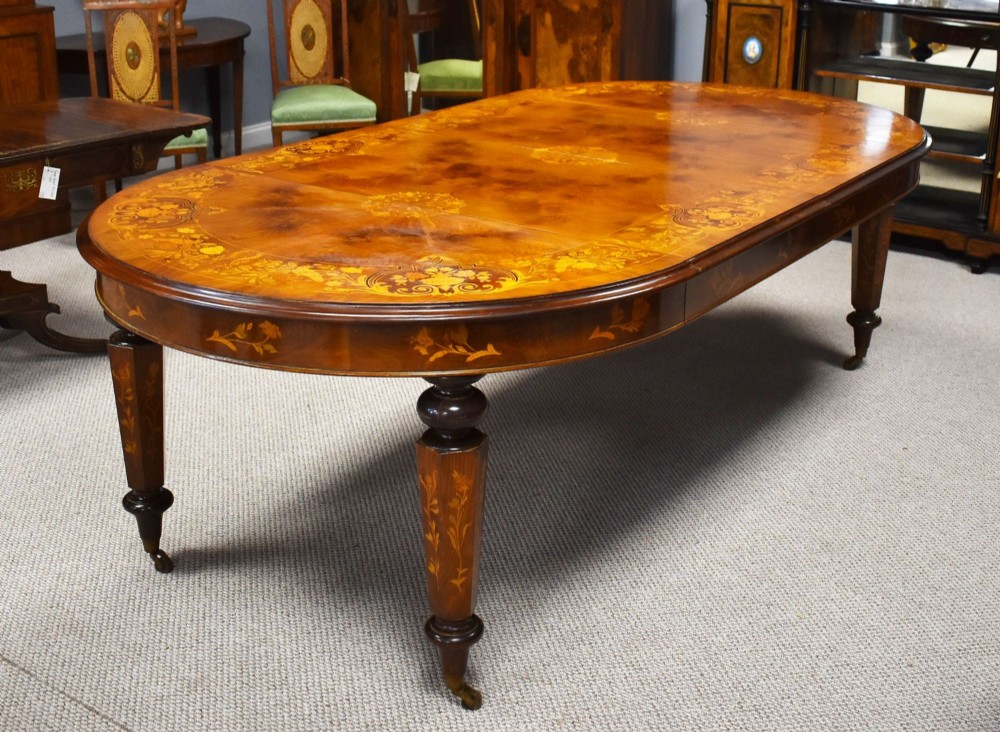 An antique Victorian walnut extending dining table featuring marquetry inlay, turned legs, and brass castors.