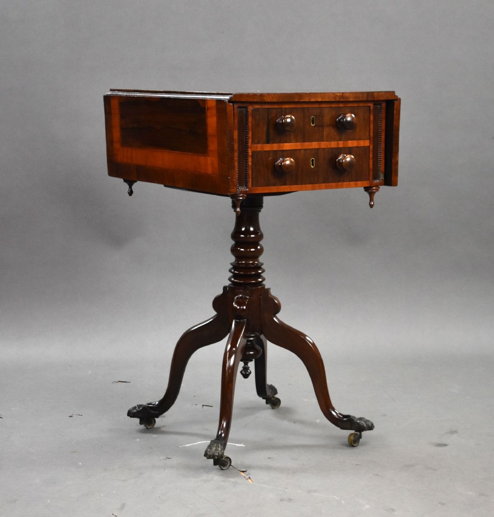 A Regency mahogany work table featuring drop leaves, two drawers with round wooden knobs, a turned central pedestal column, and four splayed legs with brass castors.