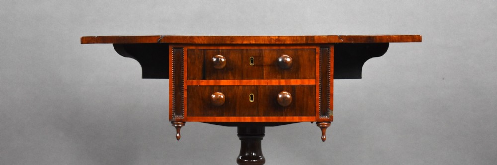 A Regency mahogany work table featuring drop leaves, two drawers with round wooden knobs, a turned central pedestal column, and four splayed legs with brass castors. View VIII