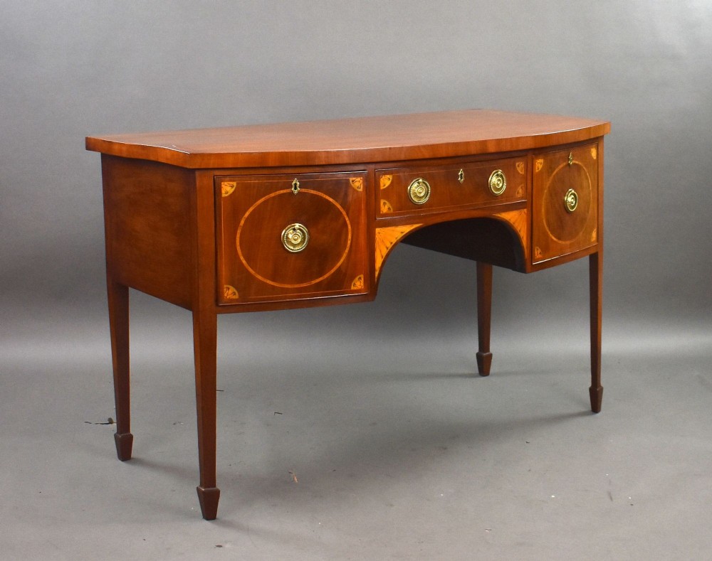 A Georgian mahogany bowfront sideboard featuring satinwood oval inlay panels, brass ring handles, and tapered square legs.