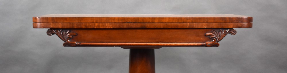A William IV mahogany card table featuring a rectangular swivel fold-over top, a tapered pedestal, and a shaped plinth base with carved scroll feet on brass castors. View VI