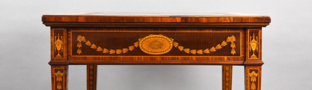 A 19th-century rectangular wooden writing desk featuring detailed marquetry swags on the apron, a leather writing surface, and four square tapered legs on brass castors. View XII