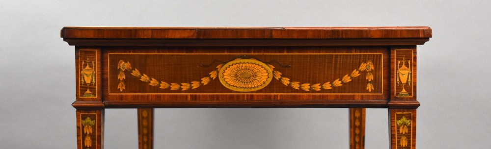 A 19th-century rectangular wooden writing desk featuring detailed marquetry swags on the apron, a leather writing surface, and four square tapered legs on brass castors. View XV