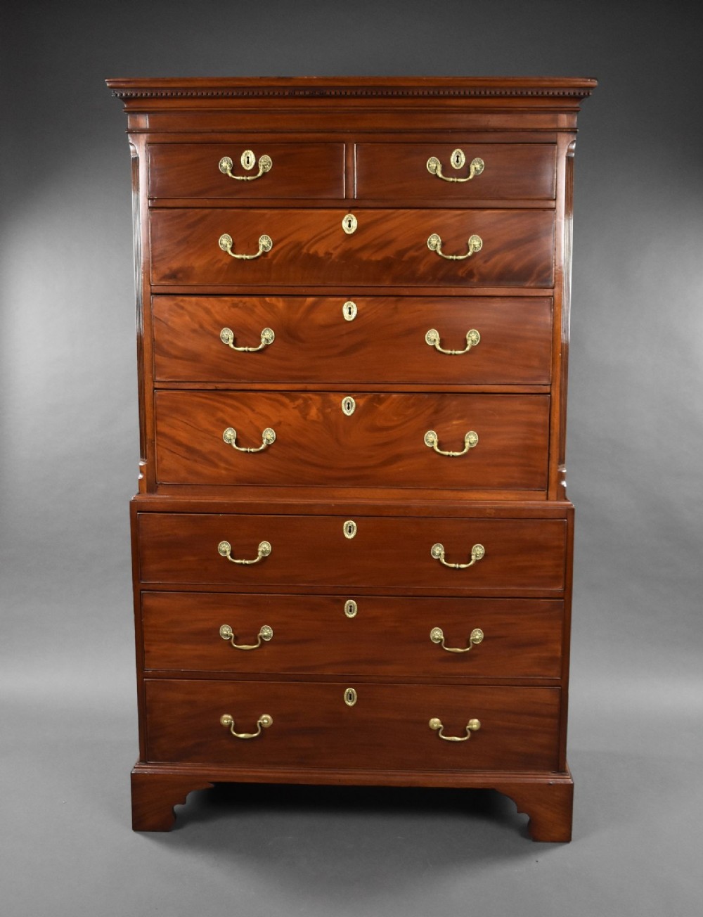 A George III mahogany chest on chest featuring multiple stacked drawers with flame mahogany veneer, brass handles, and bracket feet.