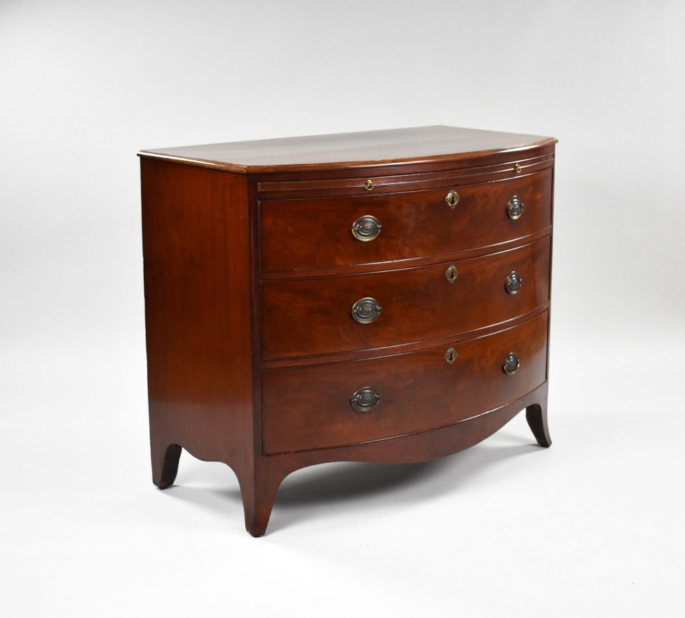 A Regency mahogany bow-front chest of drawers featuring three graduated drawers with brass oval handles and splayed bracket feet.