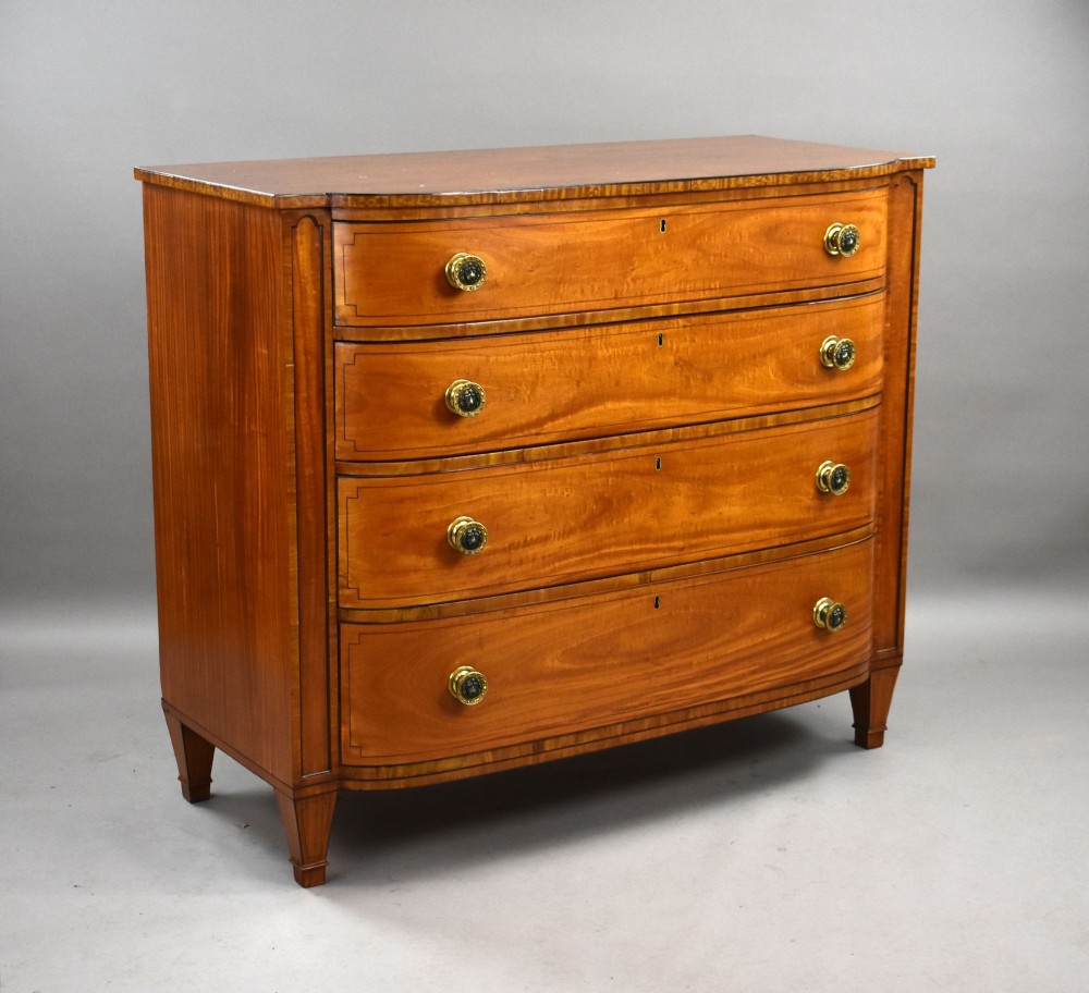 A Regency period bowfront chest of four graduated drawers constructed from golden satinwood with crossbanded borders and turned brass knobs.