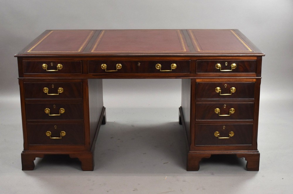 An Edwardian mahogany pedestal desk featuring a three-panel red gilt-tooled leather writing top, nine drawers with brass handles, and bracket feet.