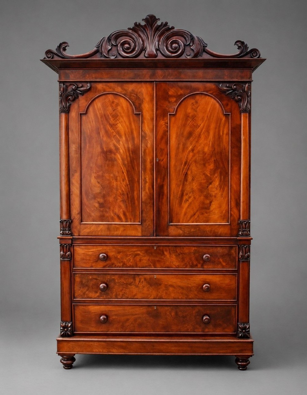 A William IV flame mahogany linen press with a carved scroll cresting, double arched panel doors, and a lower chest of drawers on turned feet. View II