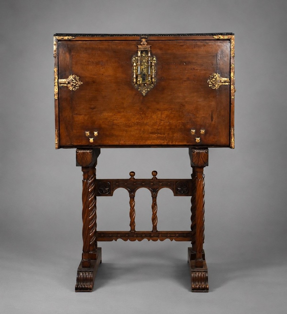A 17th-century Spanish walnut Bargueno cabinet featuring an intricate brass lockplate and side mounts, resting on an ornate barley-twist wooden stand.