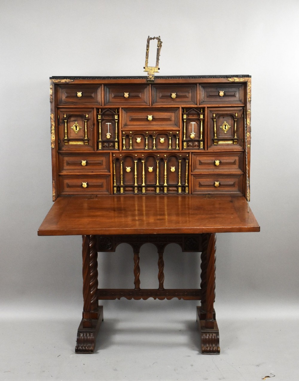 A 17th-century Spanish walnut Bargueno cabinet featuring an intricate brass lockplate and side mounts, resting on an ornate barley-twist wooden stand. View IV