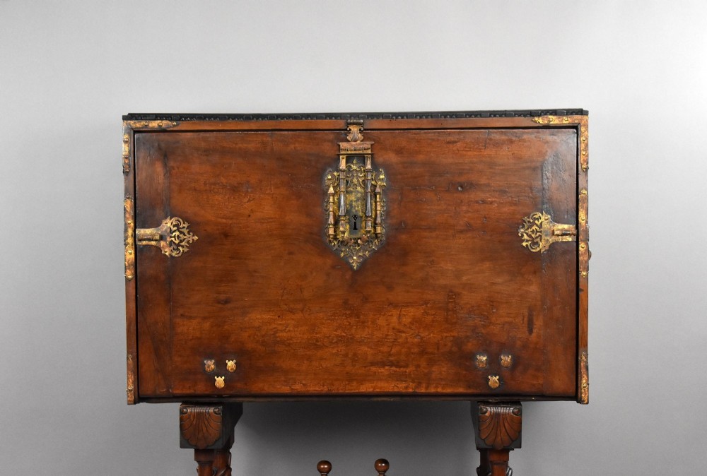 A 17th-century Spanish walnut Bargueno cabinet featuring an intricate brass lockplate and side mounts, resting on an ornate barley-twist wooden stand. View V