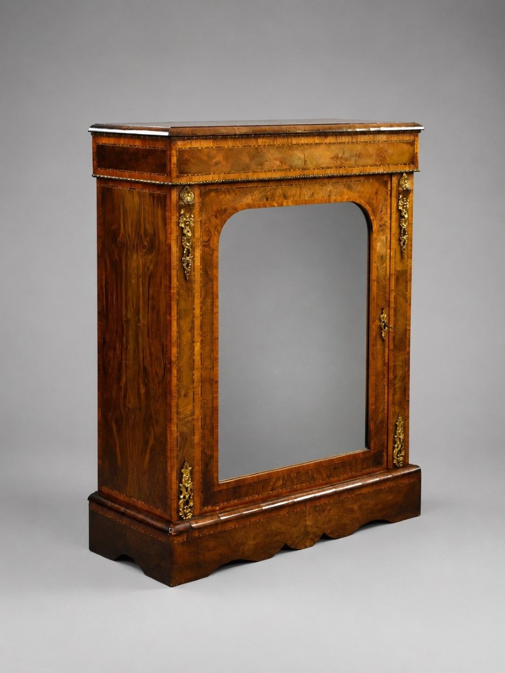 A Victorian burr walnut pier cabinet featuring a single glazed door, boxwood marquetry stringing, and ornate gilt brass mounts.