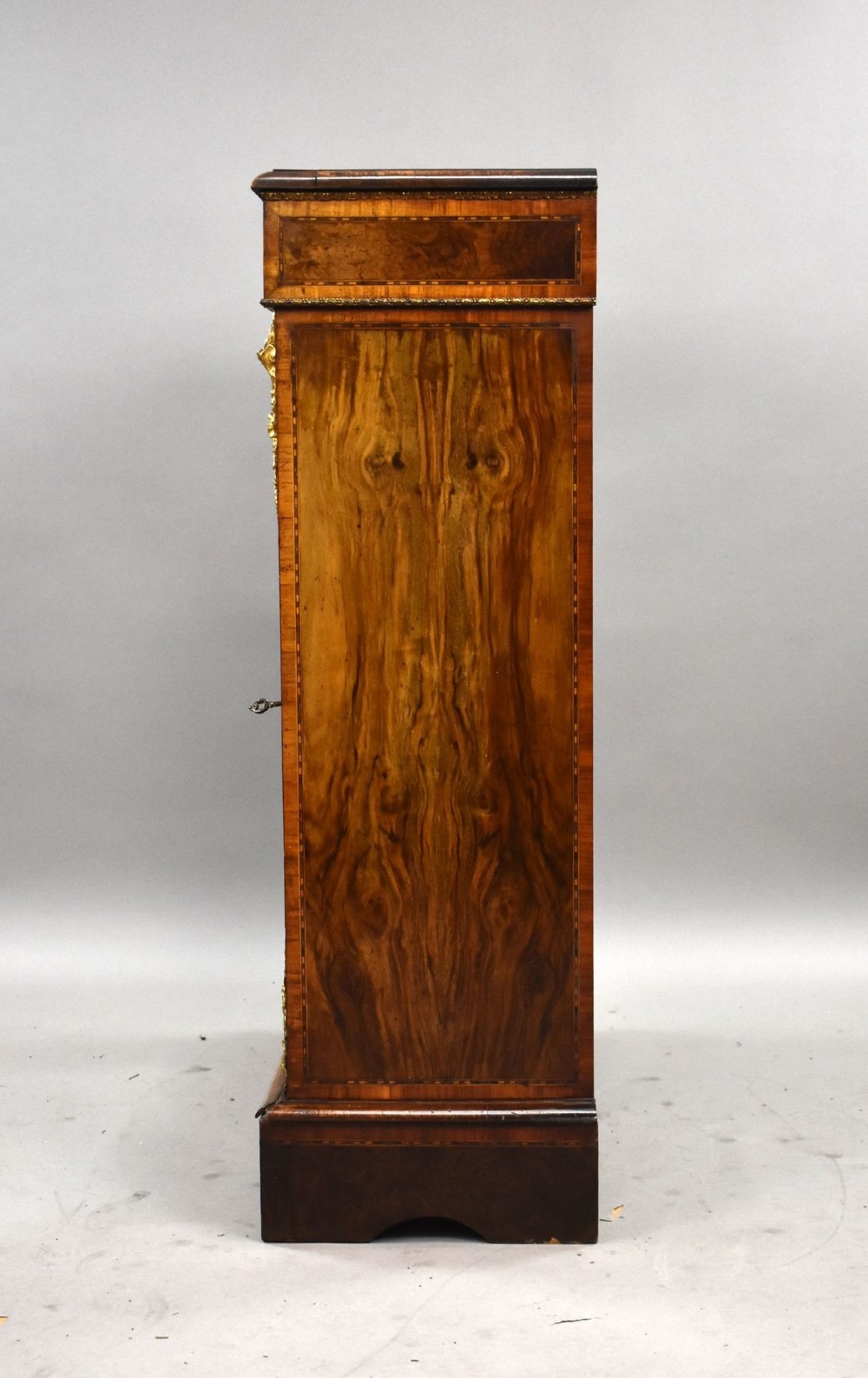 A Victorian burr walnut pier cabinet featuring a single glazed door, boxwood marquetry stringing, and ornate gilt brass mounts. View IV