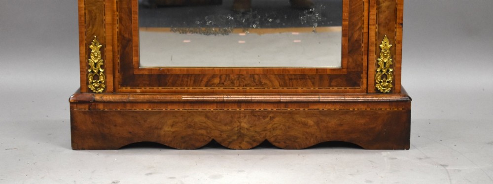 A Victorian burr walnut pier cabinet featuring a single glazed door, boxwood marquetry stringing, and ornate gilt brass mounts. View VI
