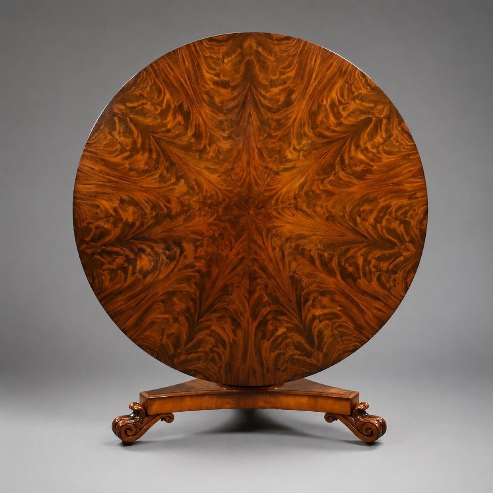 A circular William IV flame mahogany tilt-top breakfast table with a starburst veneer pattern shown in a vertical tilted position on a triform pedestal base with carved scroll feet.