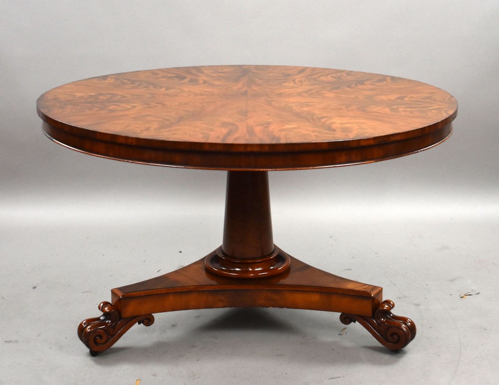 A circular William IV flame mahogany tilt-top breakfast table with a starburst veneer pattern shown in a vertical tilted position on a triform pedestal base with carved scroll feet. View III