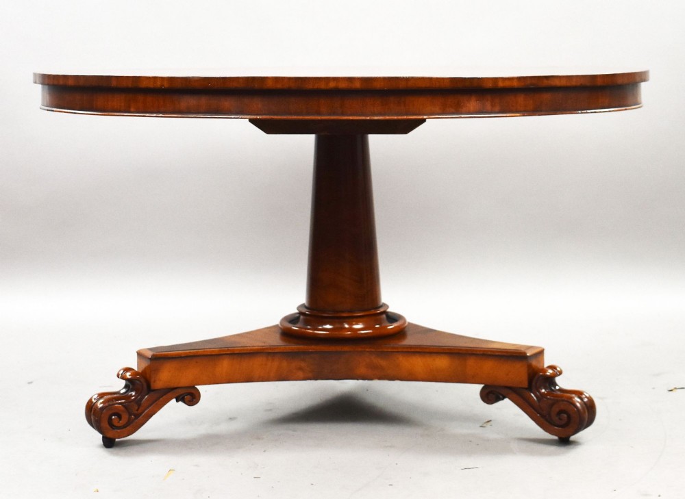 A circular William IV flame mahogany tilt-top breakfast table with a starburst veneer pattern shown in a vertical tilted position on a triform pedestal base with carved scroll feet. View IV