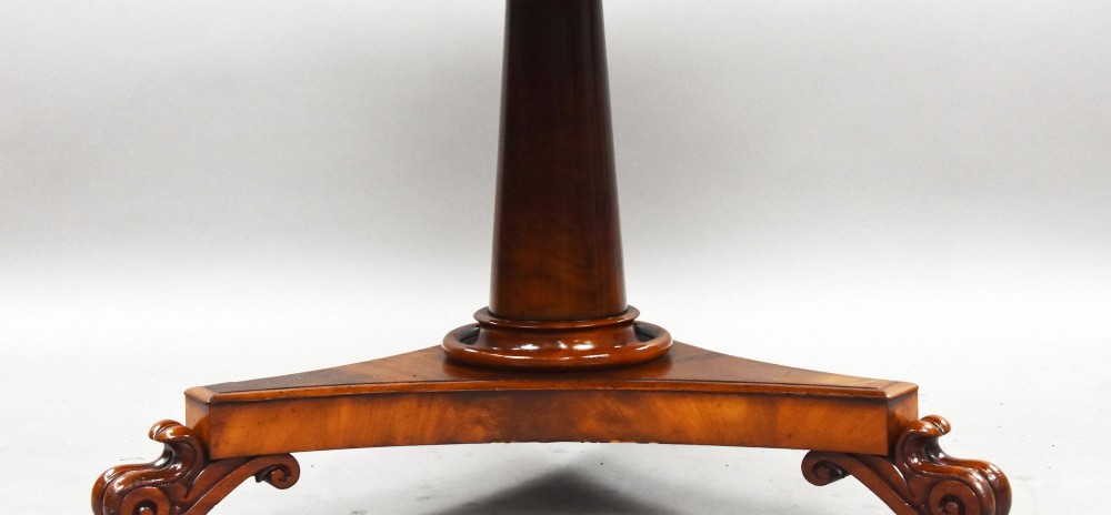 A circular William IV flame mahogany tilt-top breakfast table with a starburst veneer pattern shown in a vertical tilted position on a triform pedestal base with carved scroll feet. View V