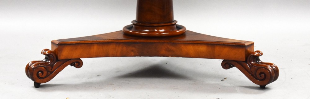 A circular William IV flame mahogany tilt-top breakfast table with a starburst veneer pattern shown in a vertical tilted position on a triform pedestal base with carved scroll feet. View VI