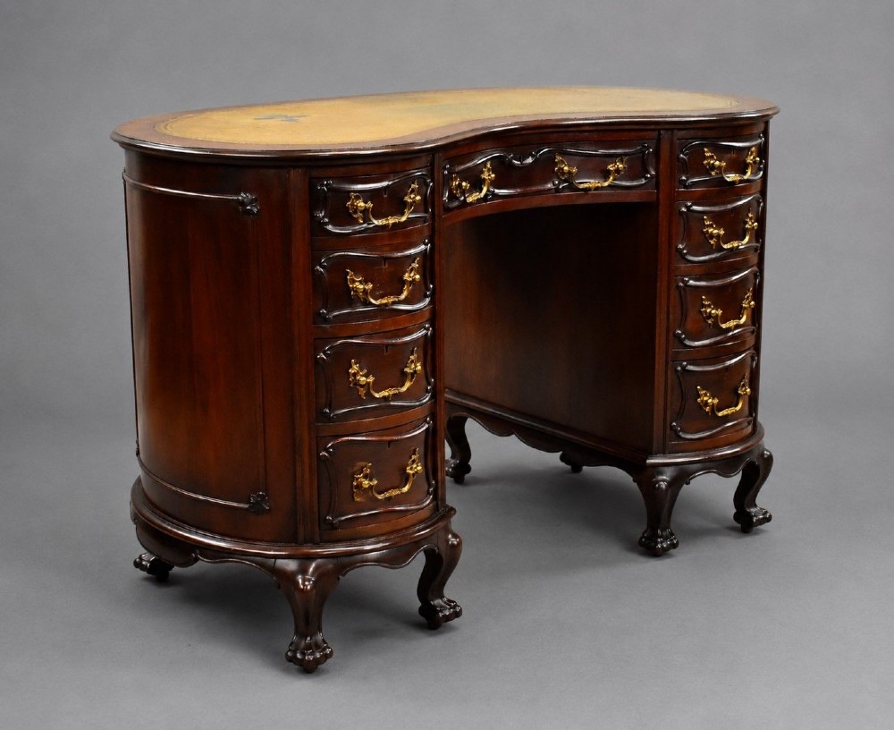 A dark mahogany kidney-shaped writing desk with a gilded leather top insert, twin pedestals featuring ornate brass handles, and cabriole legs ending in claw-and-ball feet.