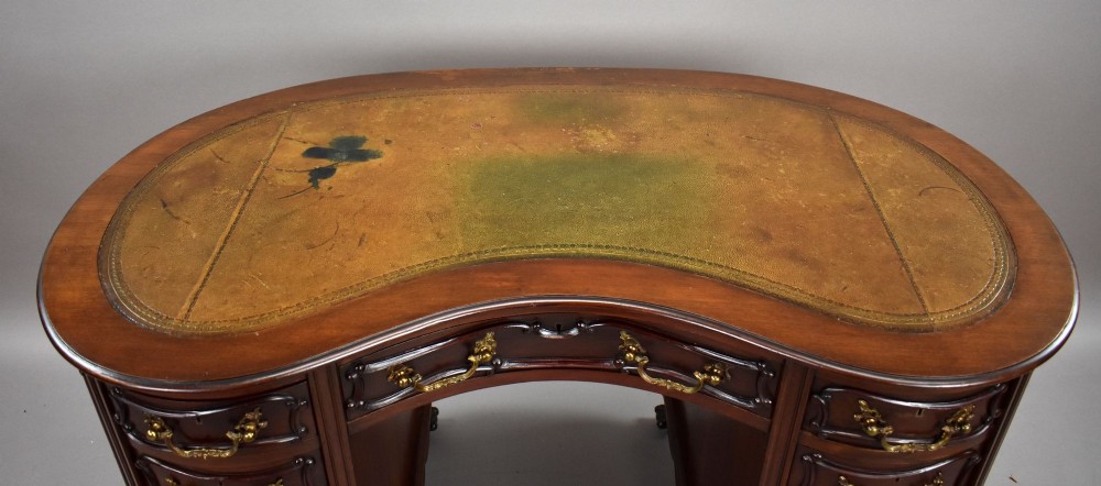 A dark mahogany kidney-shaped writing desk with a gilded leather top insert, twin pedestals featuring ornate brass handles, and cabriole legs ending in claw-and-ball feet. View VI