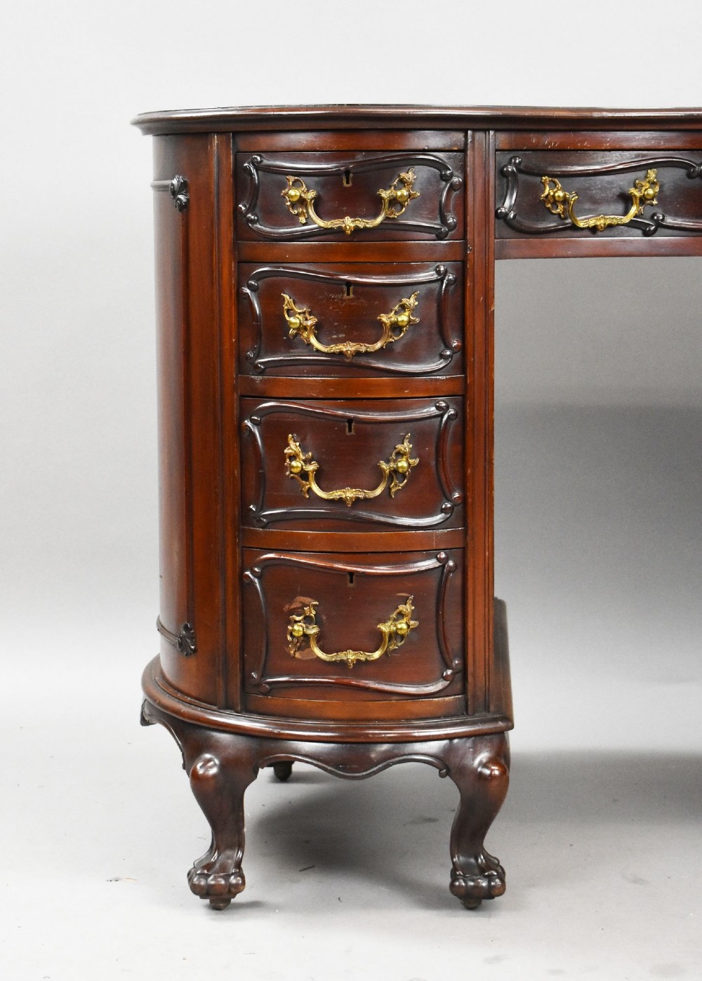 A dark mahogany kidney-shaped writing desk with a gilded leather top insert, twin pedestals featuring ornate brass handles, and cabriole legs ending in claw-and-ball feet. View VII