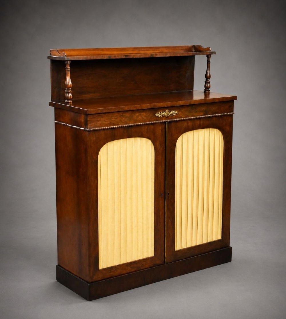 A Victorian dark rosewood chiffonier featuring an upper display shelf supported by turned pillars above lower cabinet doors fitted with pleated fabric panels.