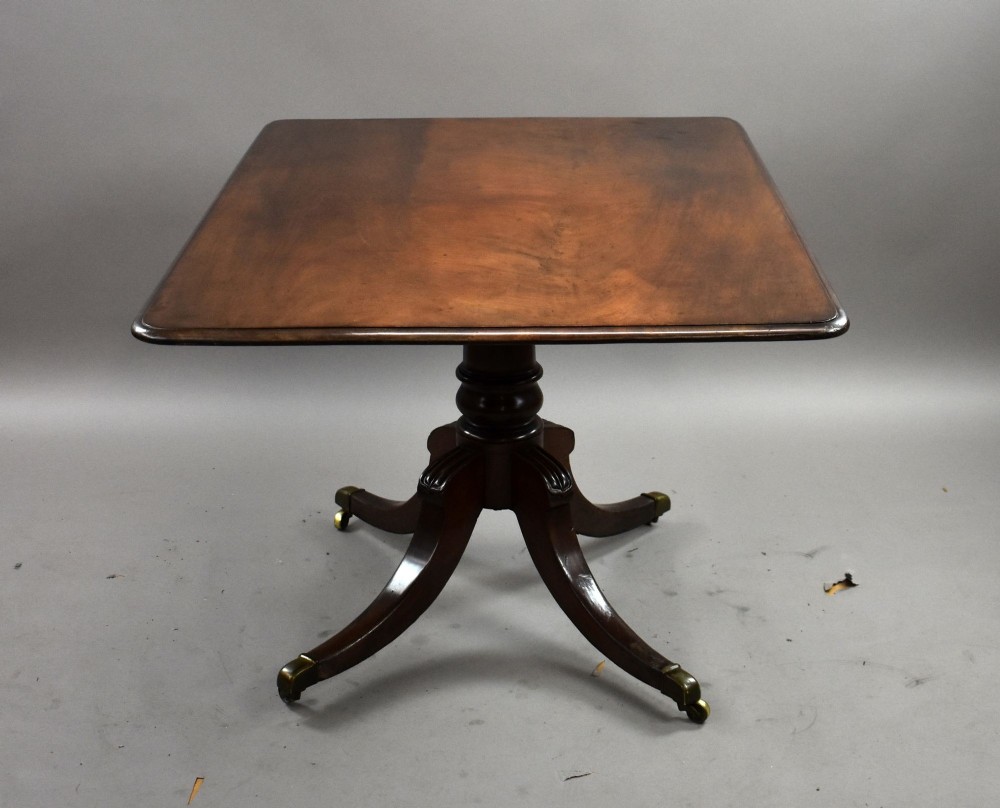 A Regency mahogany tilt-top breakfast table with its rectangular top secured in a vertical position above a pedestal base with curved splayed legs and brass castors. View II