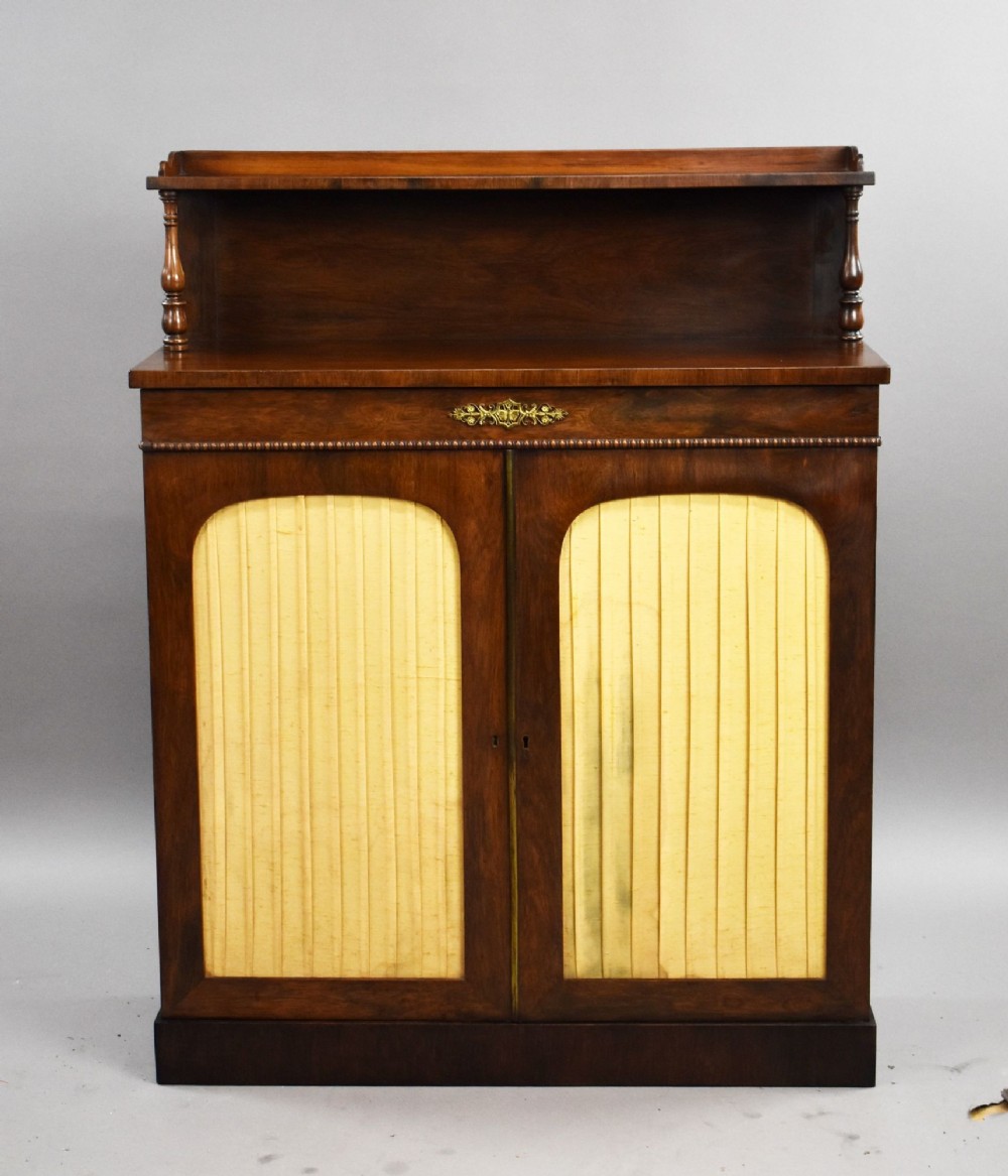 A Victorian dark rosewood chiffonier featuring an upper display shelf supported by turned pillars above lower cabinet doors fitted with pleated fabric panels. View II