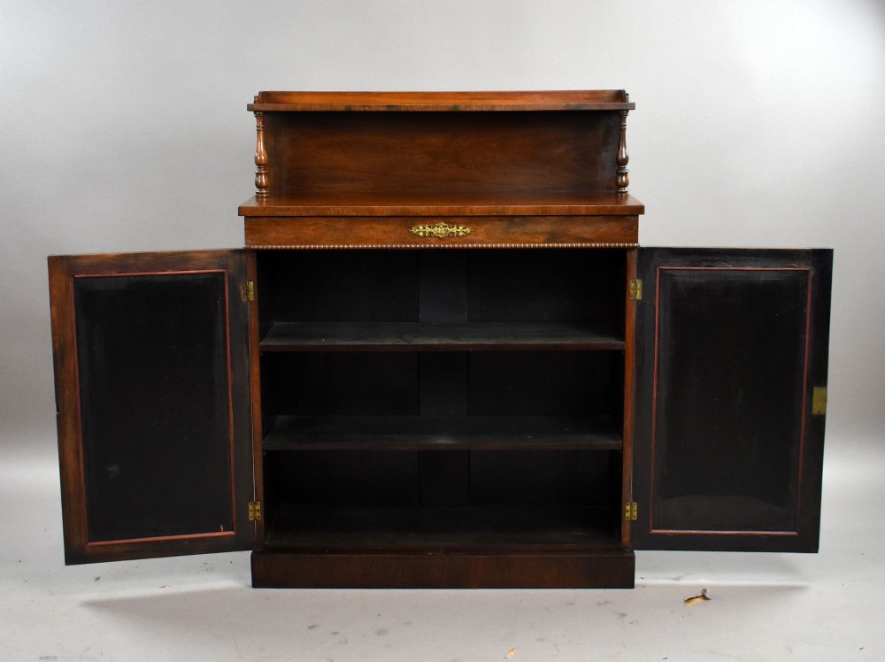 A Victorian dark rosewood chiffonier featuring an upper display shelf supported by turned pillars above lower cabinet doors fitted with pleated fabric panels. View VII