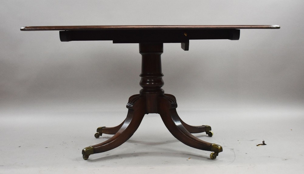 A Regency mahogany tilt-top breakfast table with its rectangular top secured in a vertical position above a pedestal base with curved splayed legs and brass castors. View III