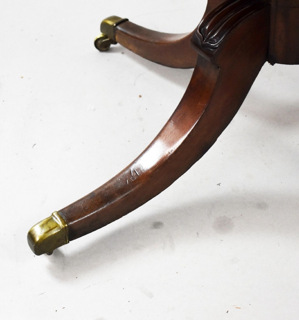 A Regency mahogany tilt-top breakfast table with its rectangular top secured in a vertical position above a pedestal base with curved splayed legs and brass castors. View IV
