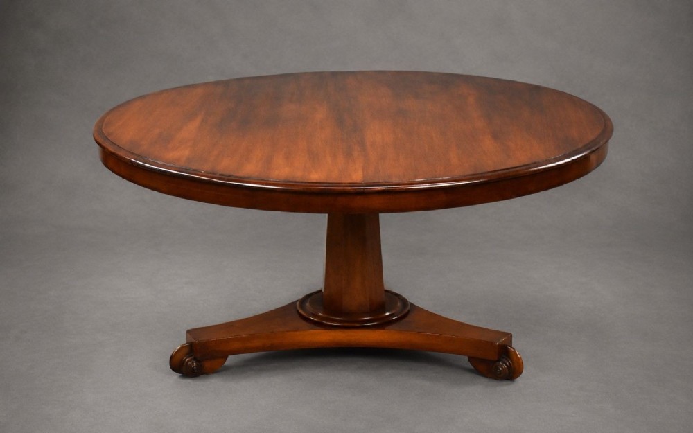 A low circular mahogany coffee table featuring a central pedestal stem on a tripartite platform base with scroll feet.
