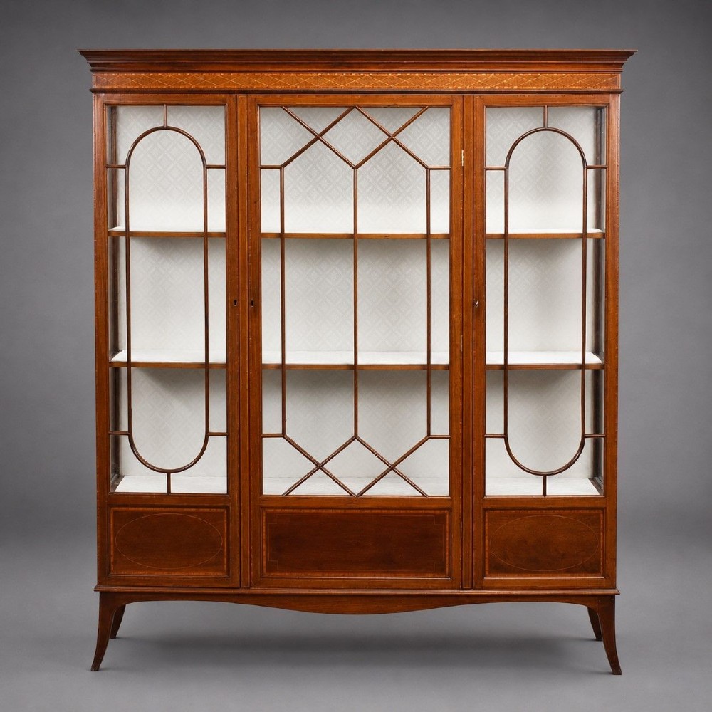 An Edwardian mahogany display cabinet featuring three glazed doors with geometric astragal glazing bars, satinwood inlay panels, and tapered legs.